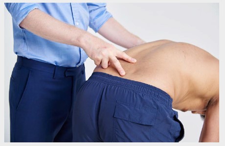 一名医生在弯下腰时检查一个男人的脊椎。